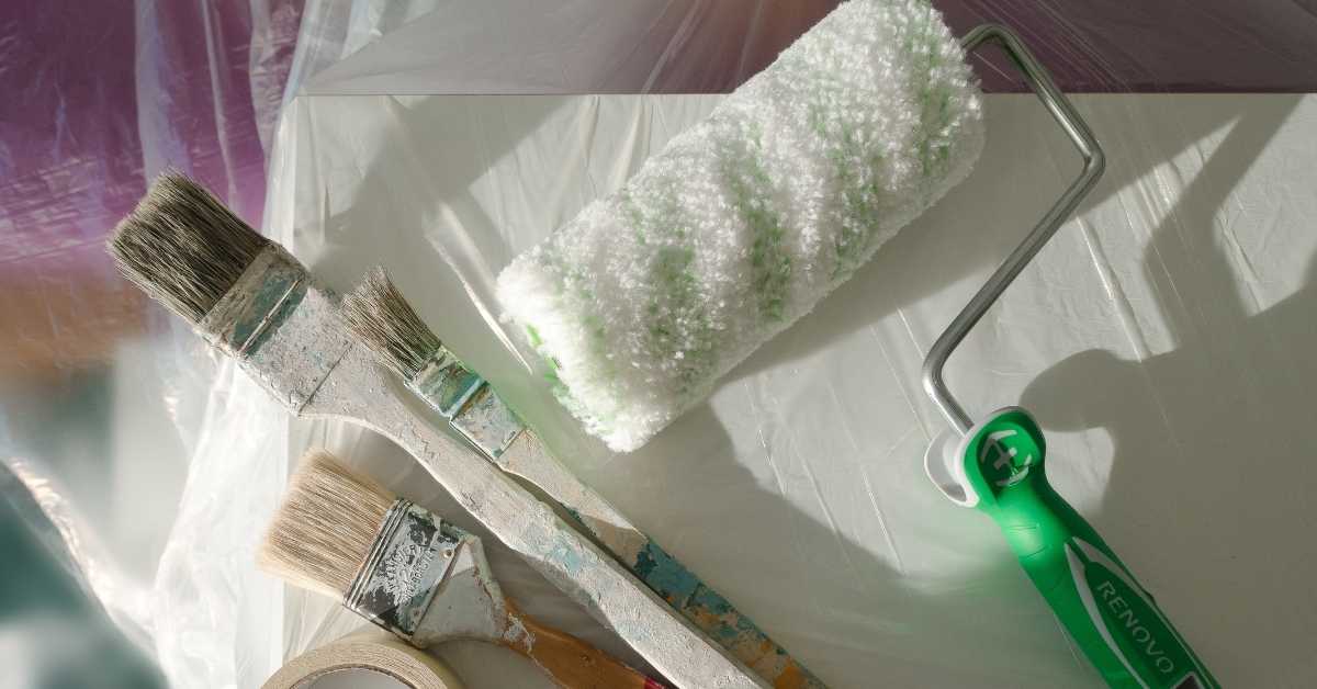 Three paint brushes and a paint roller on protective sheet