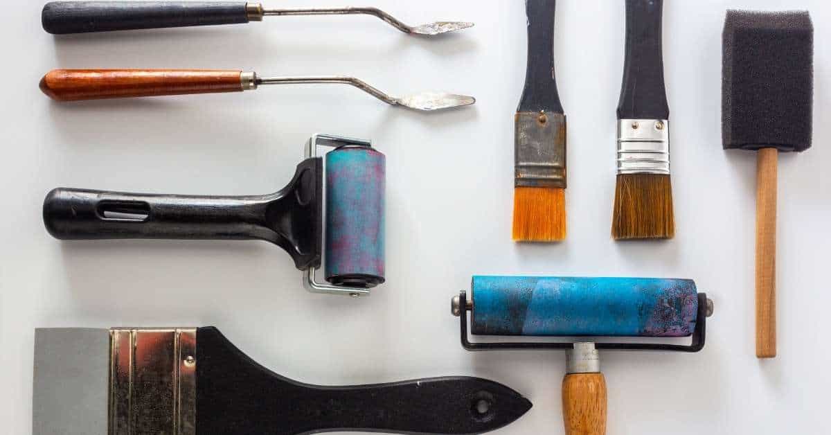 various paintbrushes rollers scrapers and tools on white background