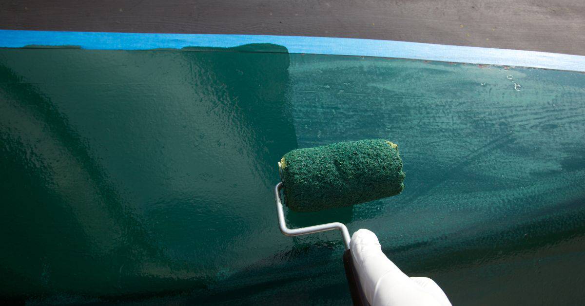 Hand with roller applying green paint on surface with tape edge