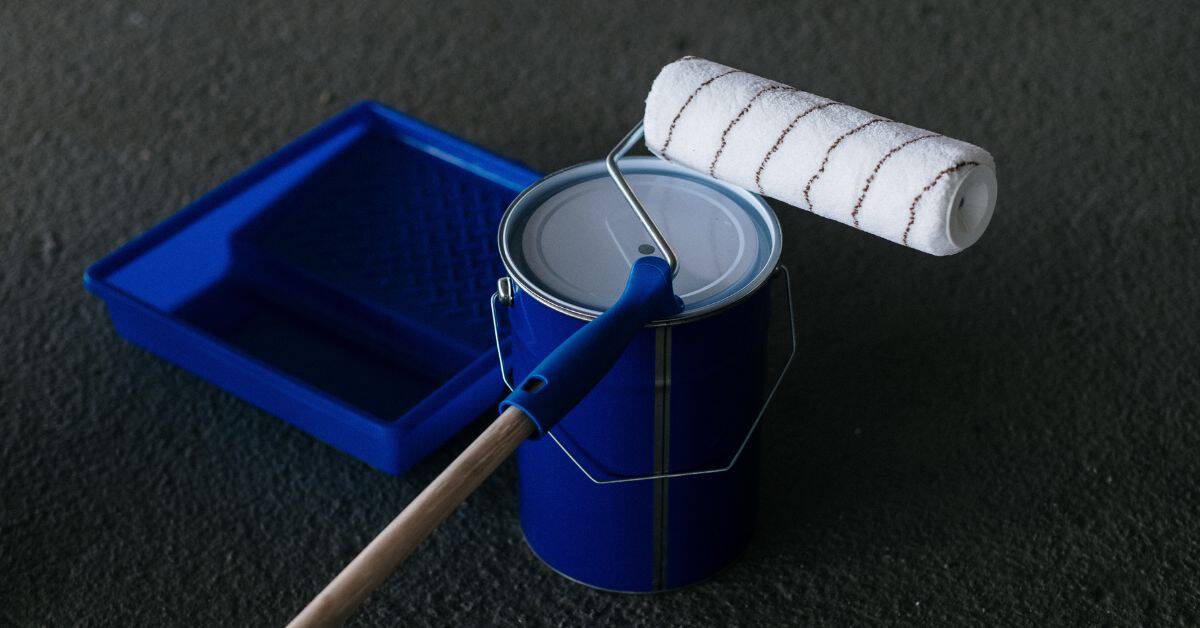 Blue paint can with roller and blue paint tray on dark surface