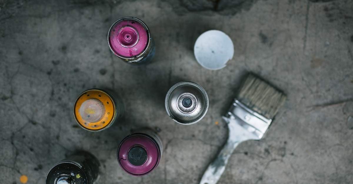 Top view of spray paint cans and paintbrush on concrete surface