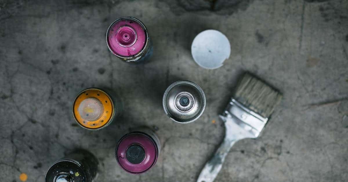 Top view of spray paint cans and paintbrush on concrete floor
