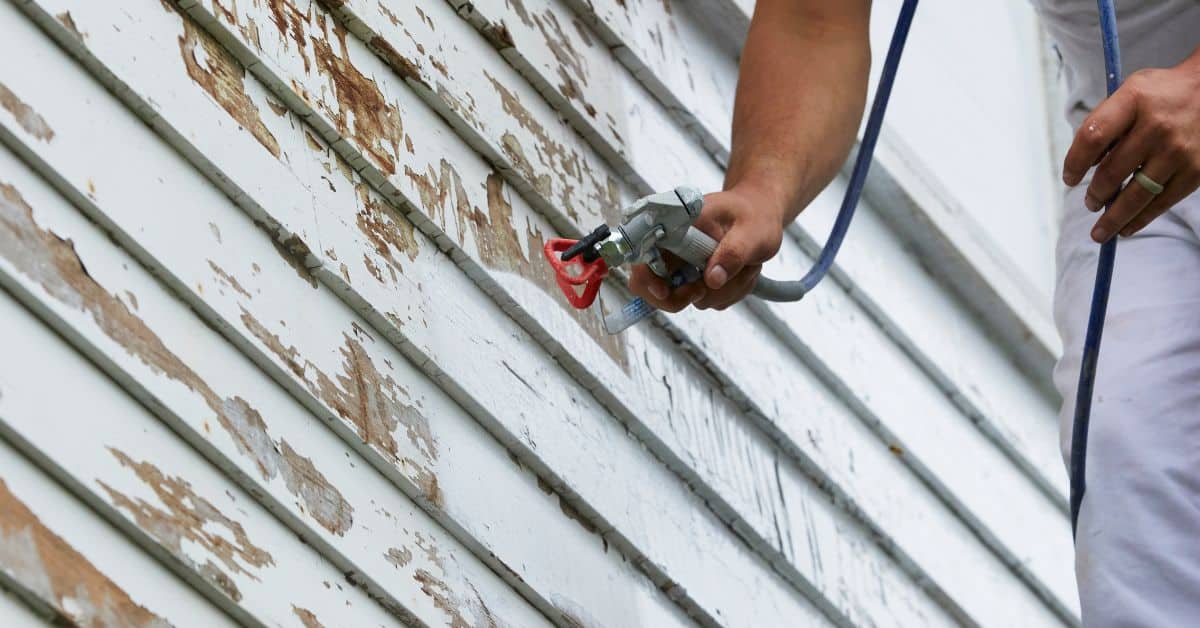 Person spraying paint or primer on peeling wood siding
