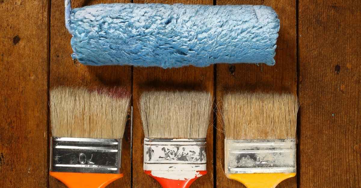 paint roller with blue paint and three paintbrushes on wooden surface