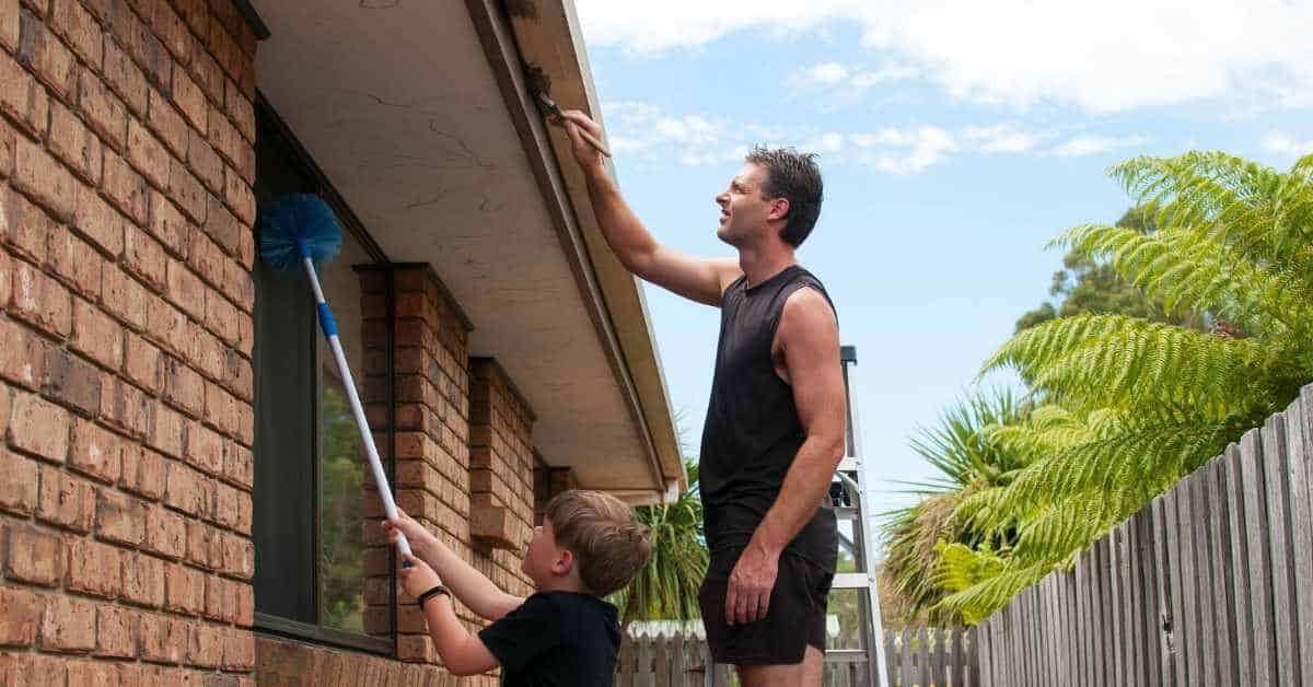 Man and child cleaning house exterior under eaves