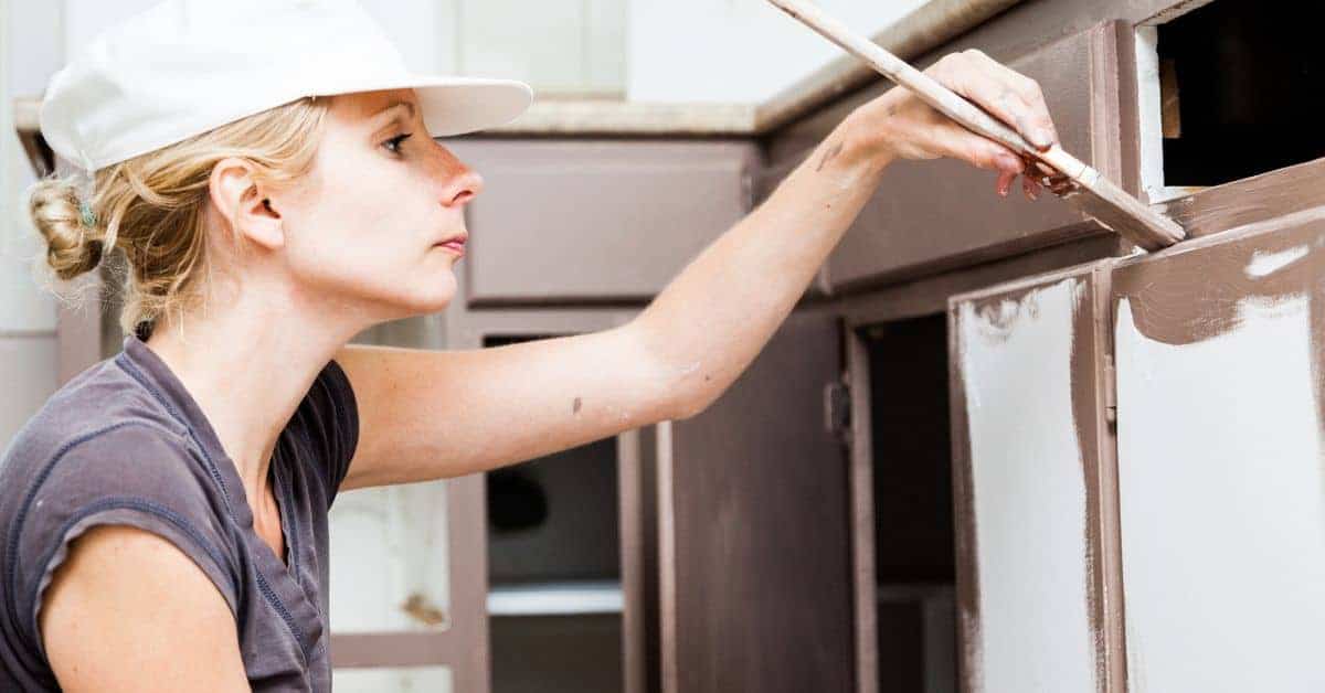 Woman painting kitchen cabinet with paintbrush