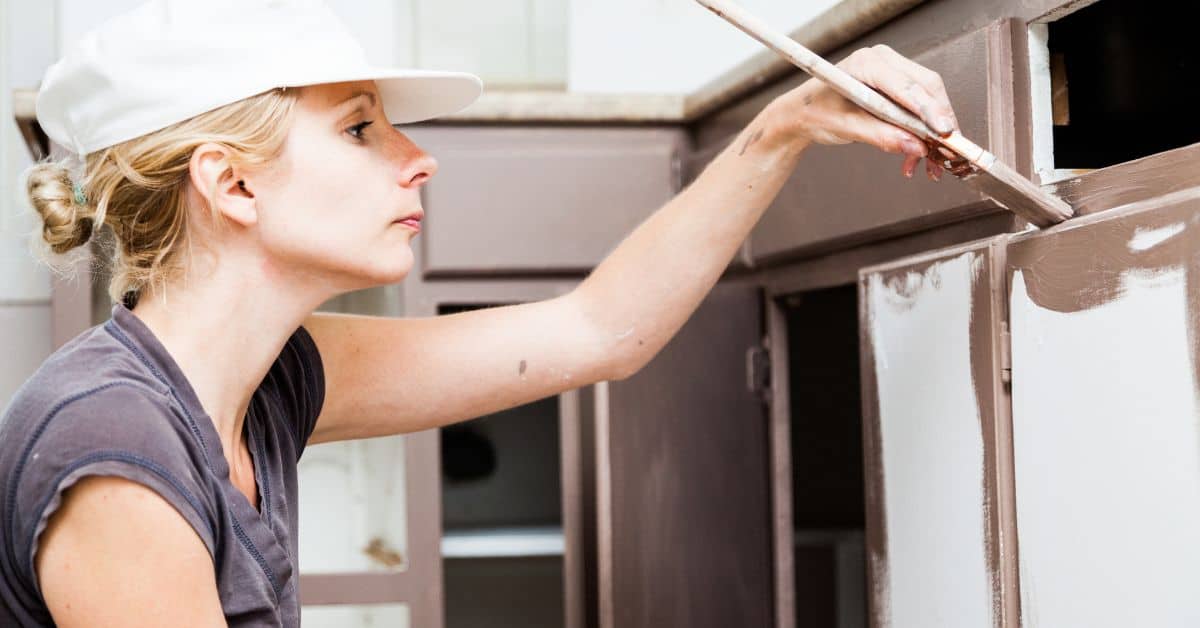 Woman painting kitchen cabinets with brown paint and brush
