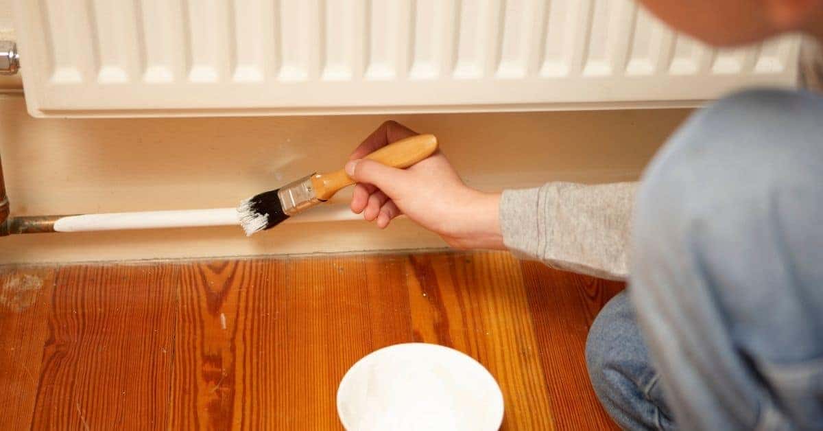Person painting a metal pipe near radiator with brush
