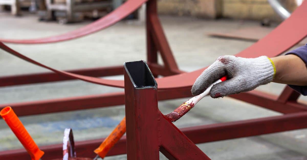 Hand wearing glove painting metal structure with brush