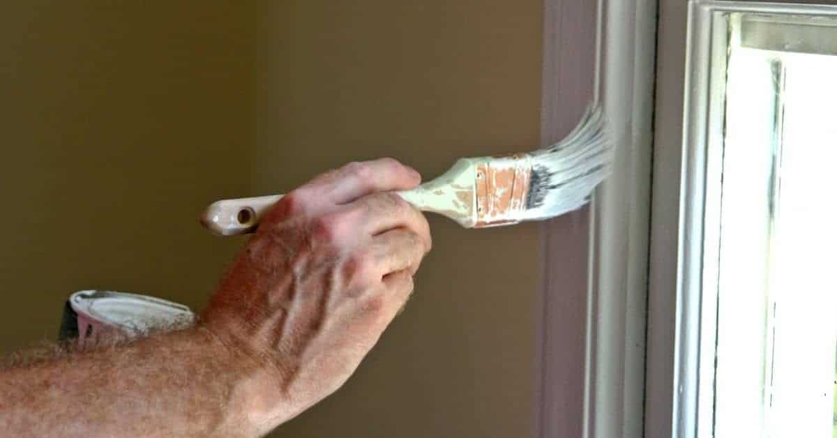 Hand painting white trim near window with brush