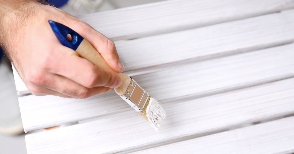 Hand painting wooden slats with white paint using small brush