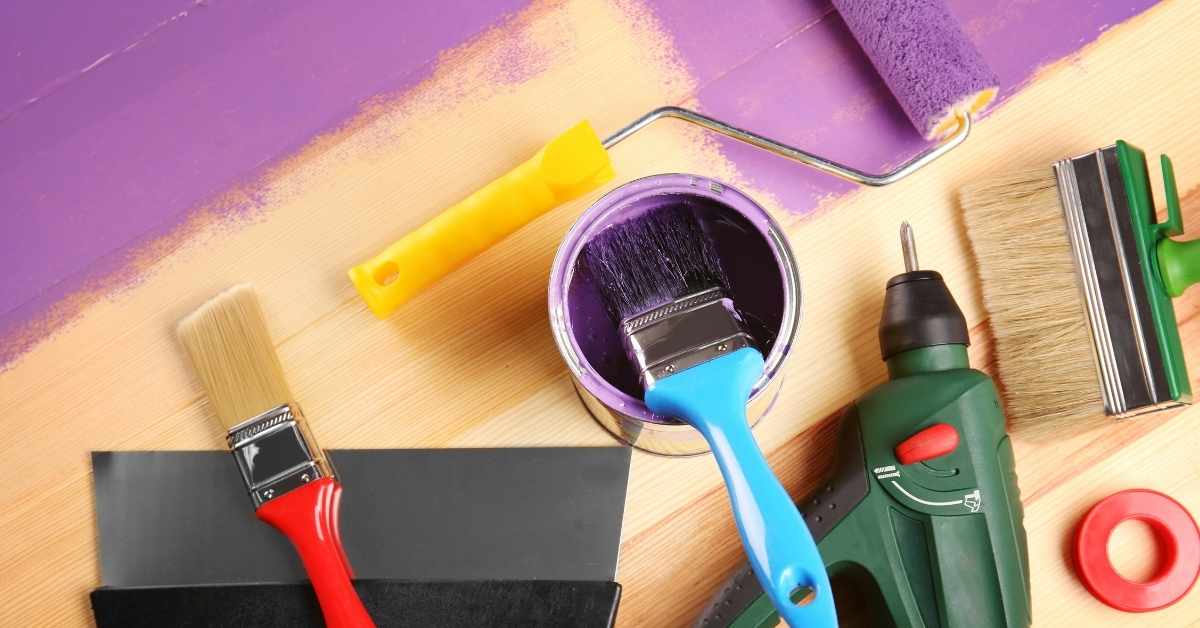 Paintbrushes roller drill putty knife and tape on wood surface