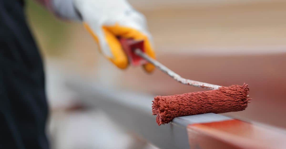 Hand with glove applying rust-colored paint with roller