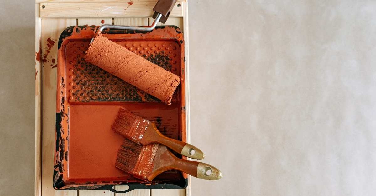 Paint roller and brushes with rust-colored paint in tray
