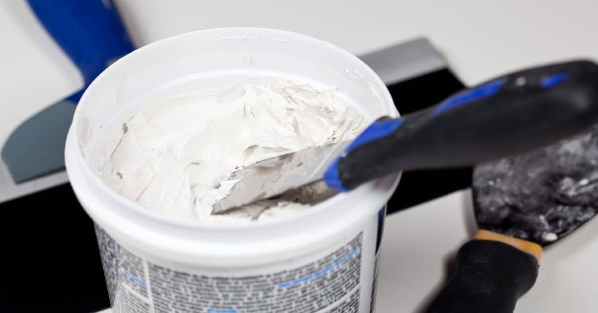 Container of white spackle with putty knife inside