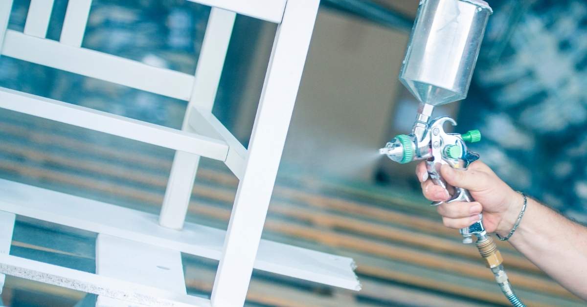 Hand spraying white paint on wooden furniture frame