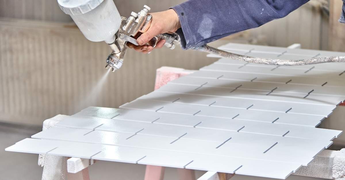 Hand spraying white paint on rectangular tiles