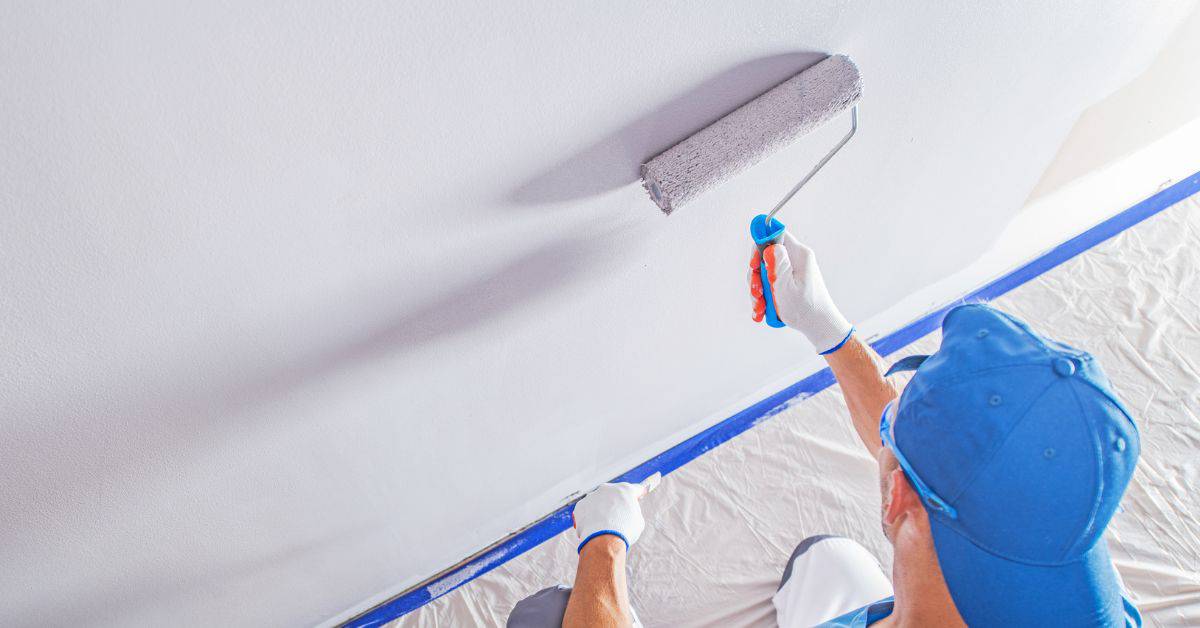 Person applying blue painter's tape along wall baseboard