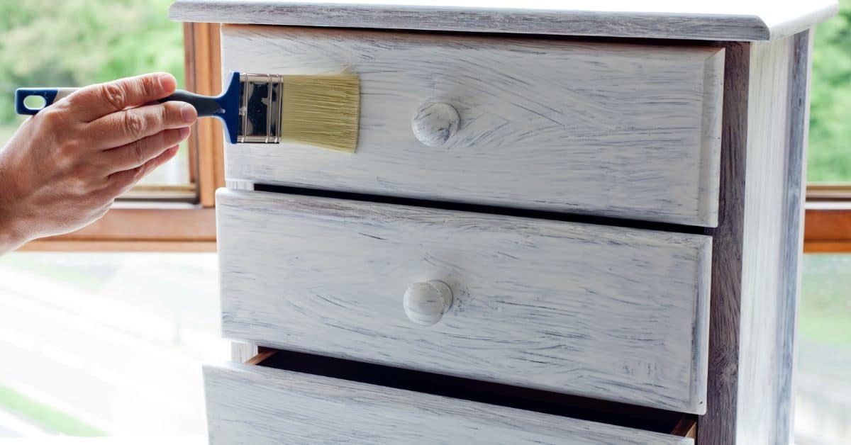 Hand brushing white paint onto wooden dresser drawer