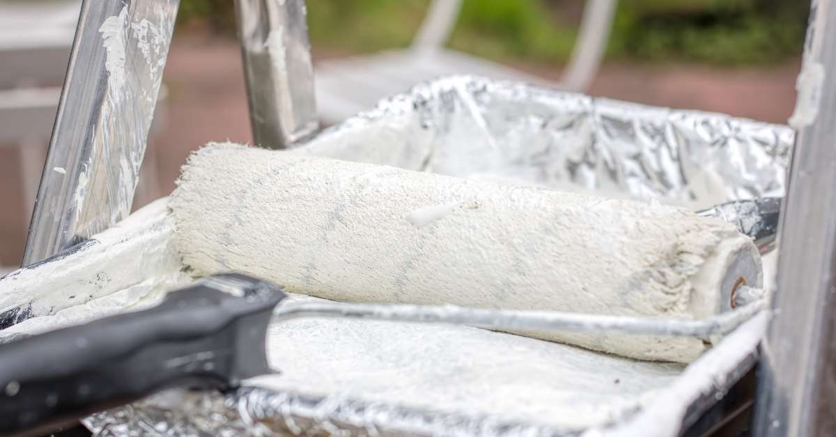 White paint roller resting in paint tray with white paint