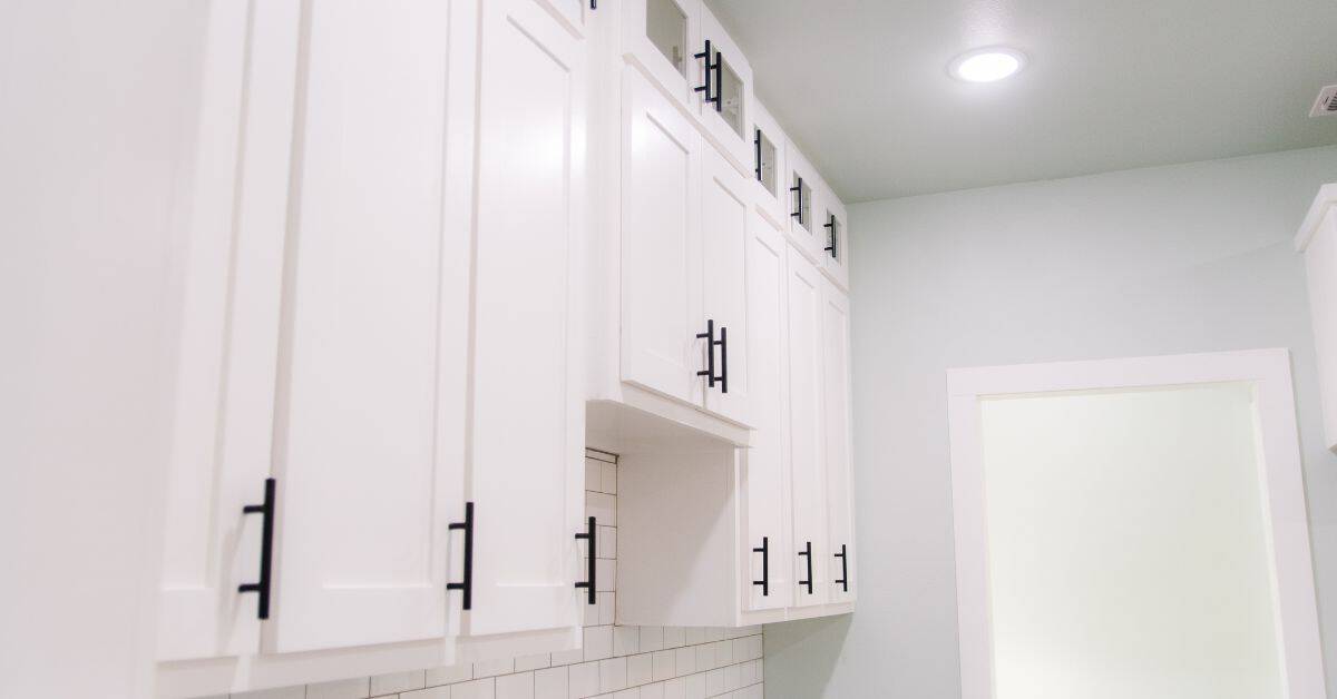 white kitchen cabinets with black handles under bright ceiling light