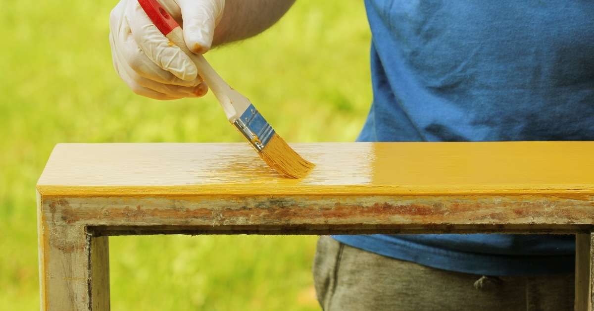 Person painting wood surface with yellow paint brush