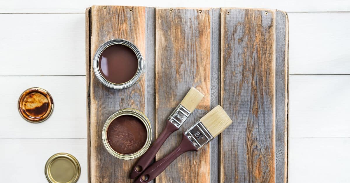 Two paintbrushes on weathered wood planks next to open paint cans