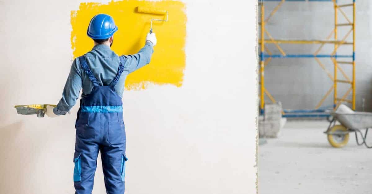 Worker in blue helmet painting wall yellow with roller