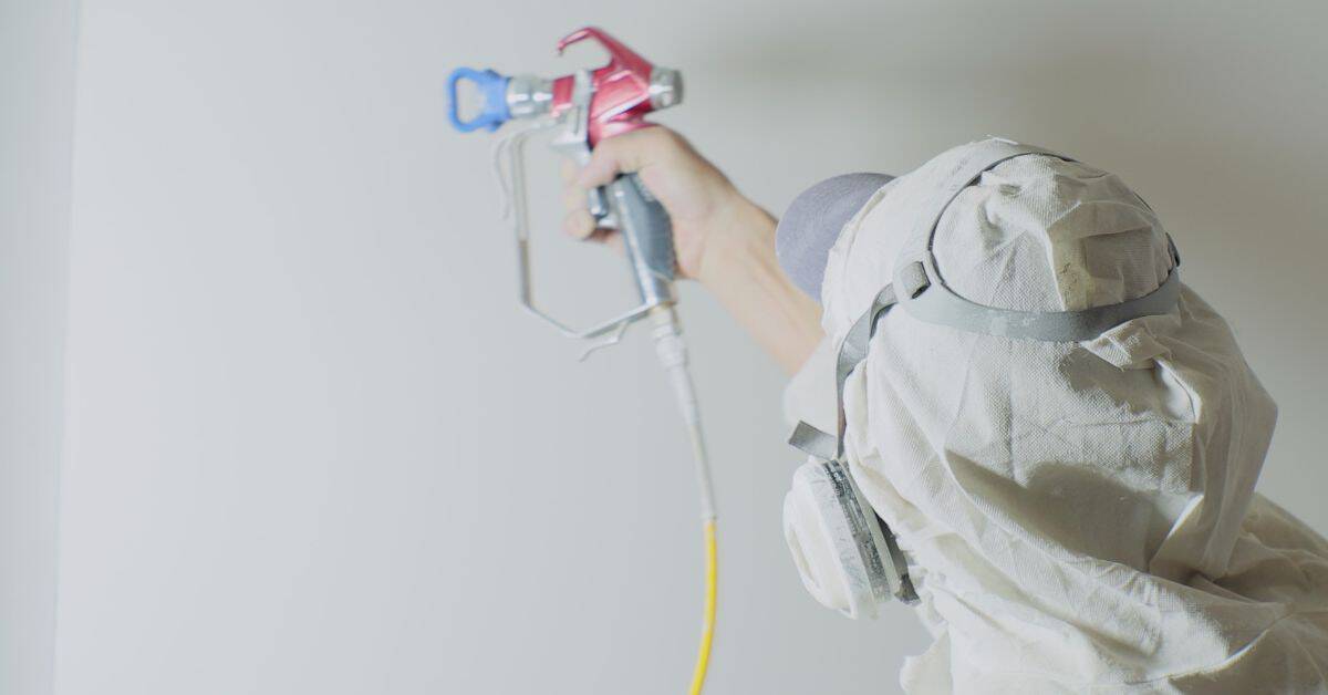 Worker in protective suit spraying paint on wall