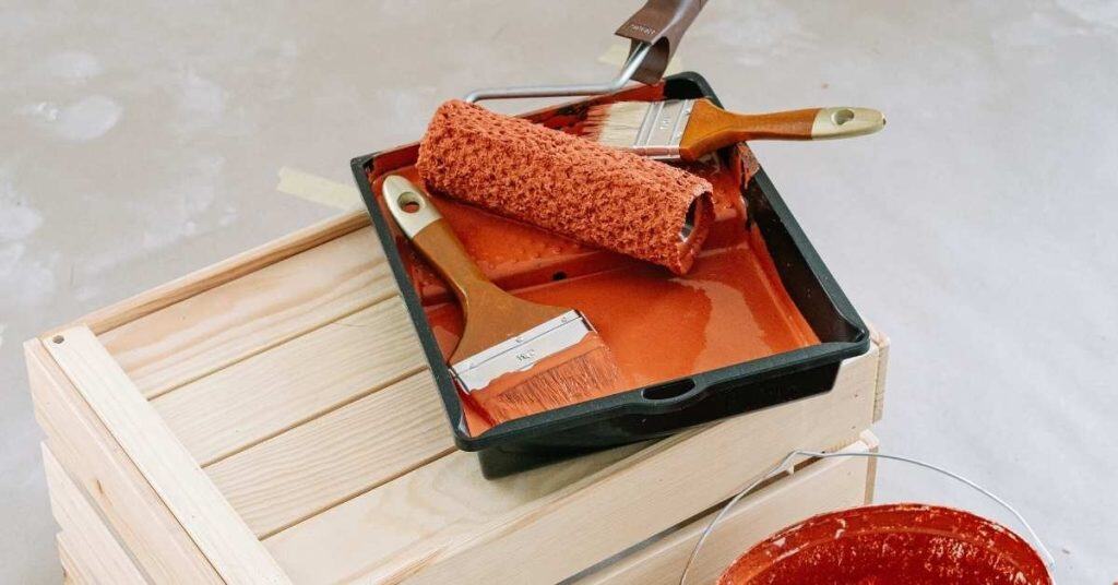 Paint roller and brushes in orange paint tray on wooden crate