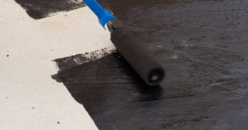 Paint roller applying black sealer on light tile surface