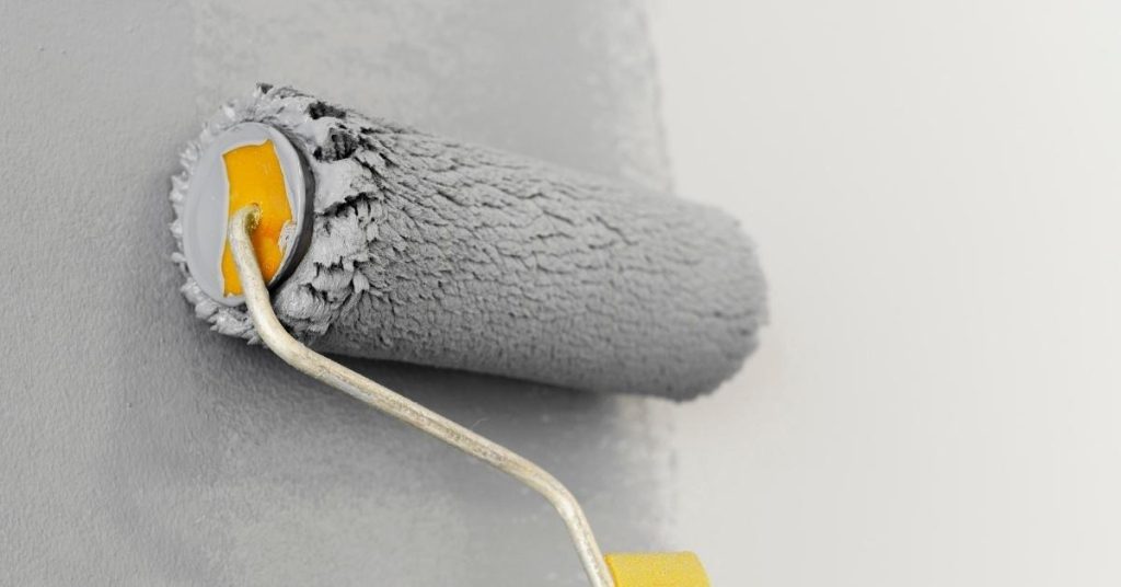 Paint roller applying gray paint on white wall