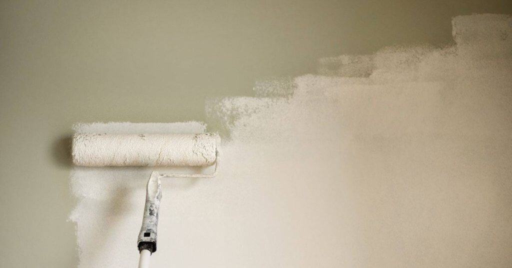 Paint roller applying white paint on beige wall