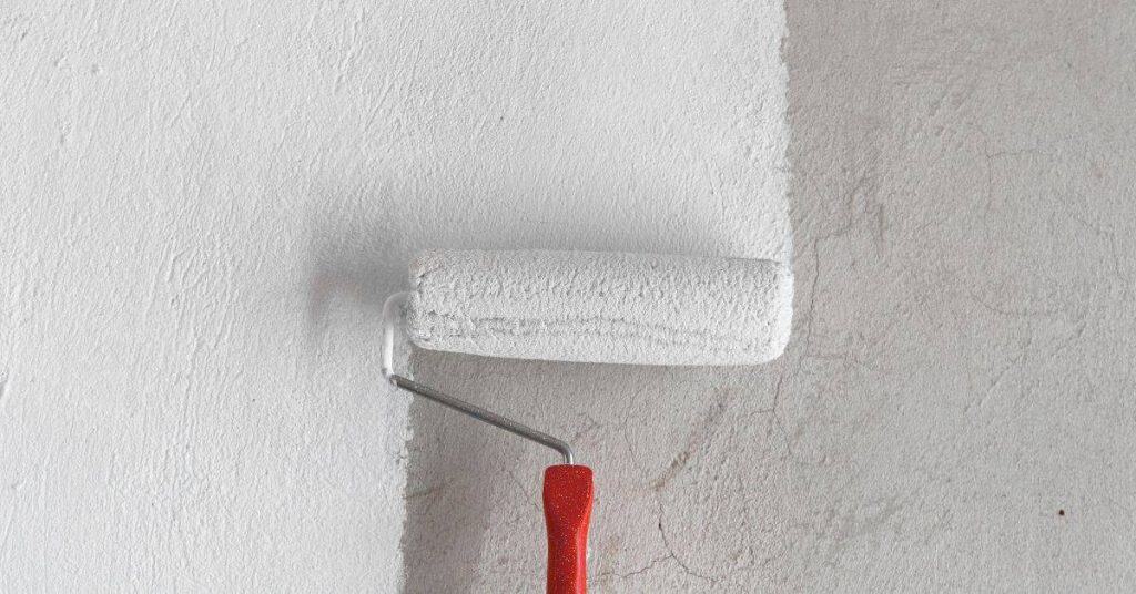 Paint roller applying white paint on textured wall surface
