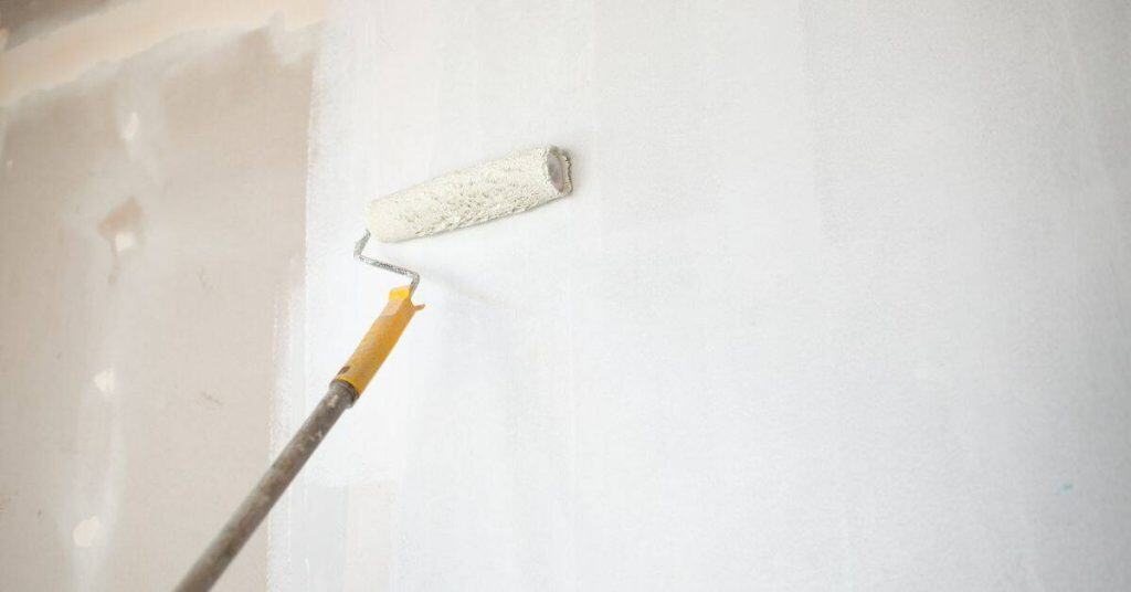 Paint roller applying white primer on drywall