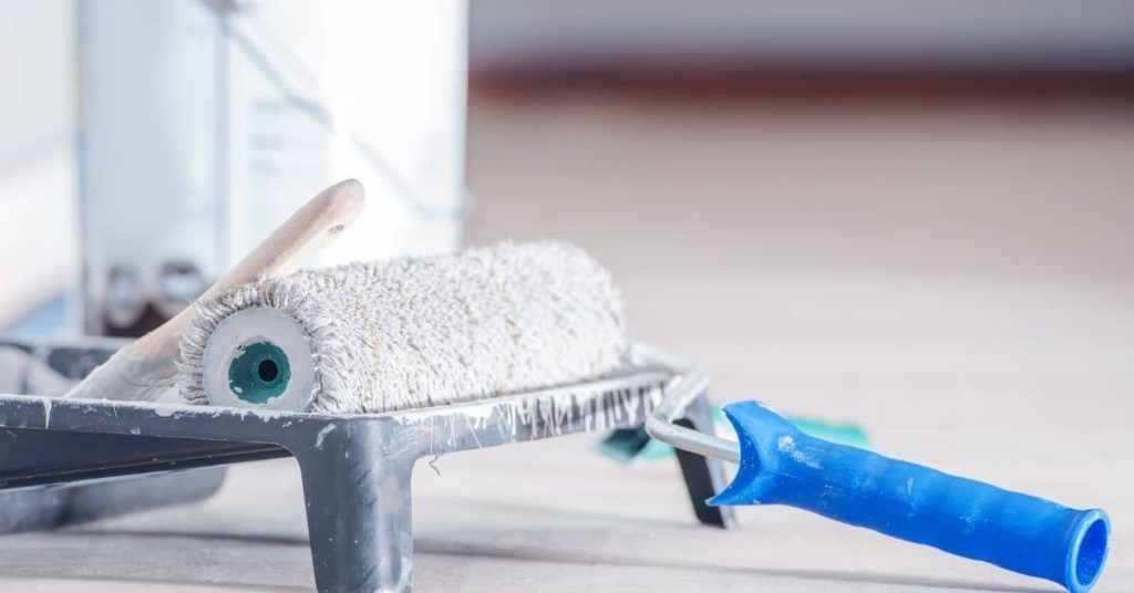 Paint roller with blue handle resting on paint tray