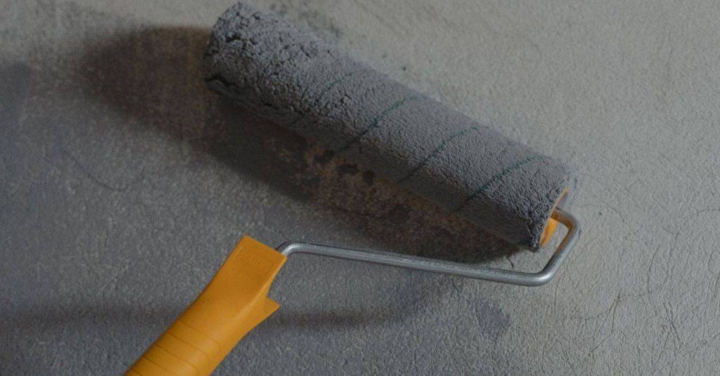 Paint roller with gray paint on textured wall surface