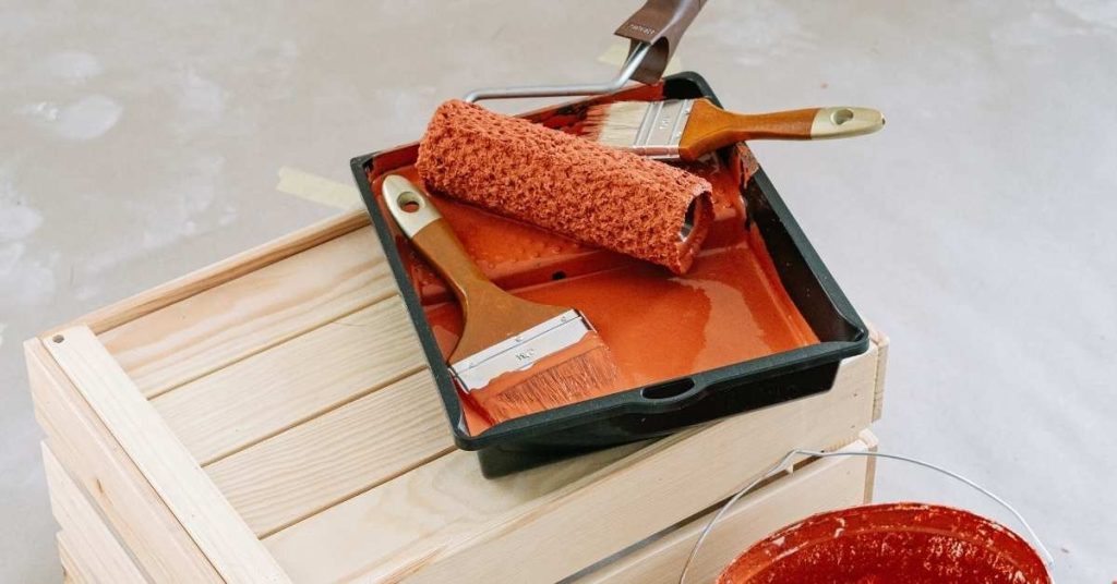 Paint tray with red paint brushes and roller on wooden crate