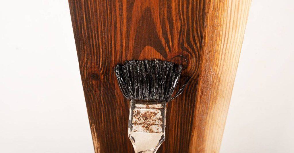 Paintbrush applying dark stain on wooden plank