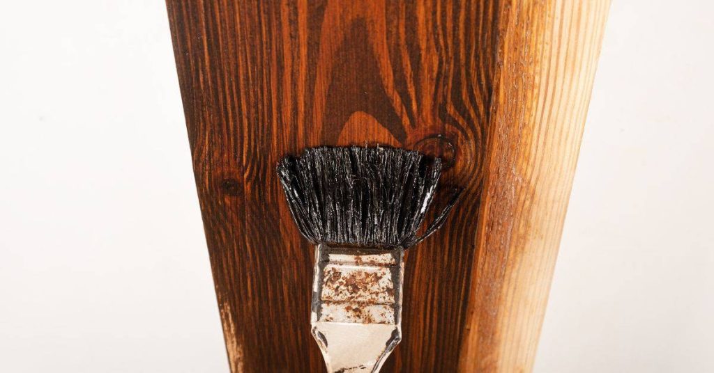 Paintbrush applying dark varnish to wooden plank