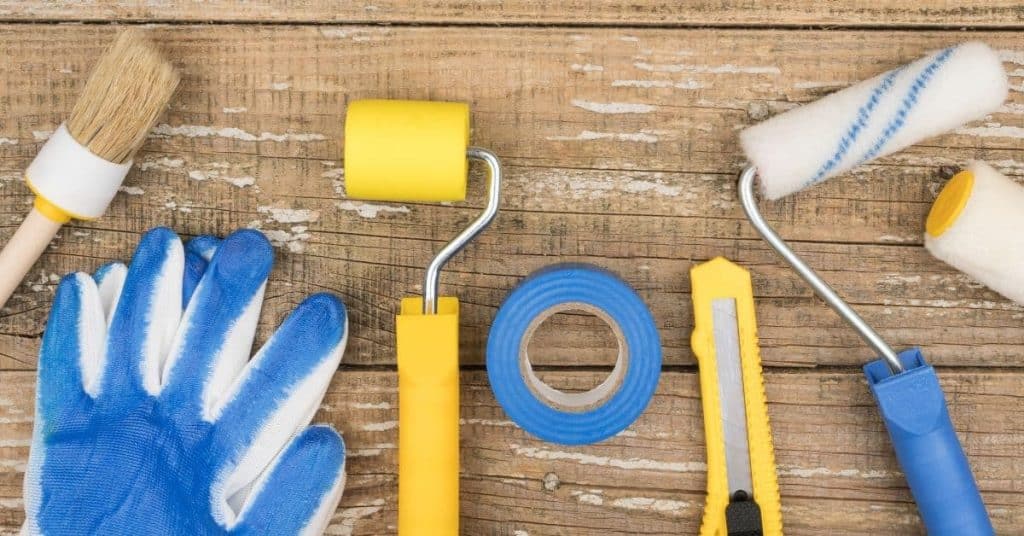Paintbrush gloves yellow rollers blue tape cutter on wood