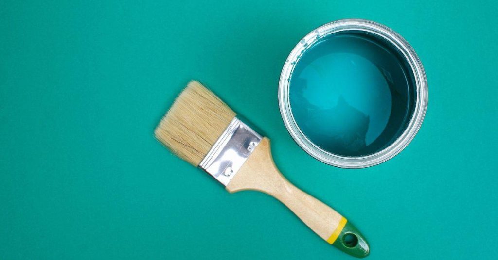 paintbrush next to an open can of blue paint