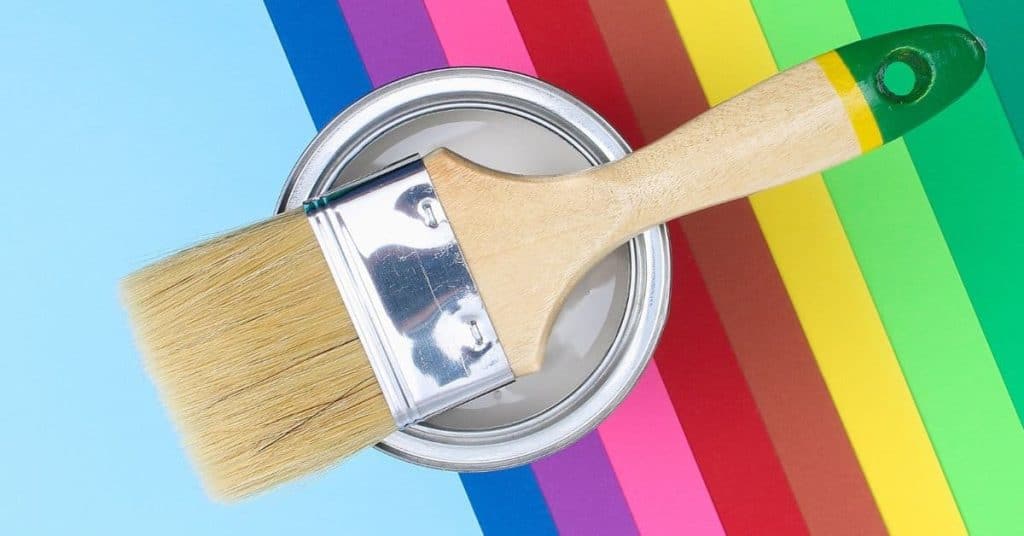 Paintbrush resting on open paint can with rainbow background