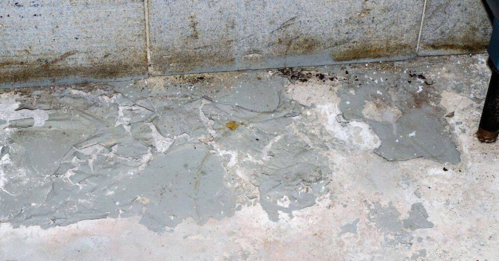 Peeling gray coating on concrete surface near wall