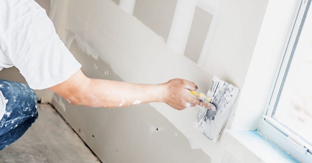 Person applying drywall joint compound near window