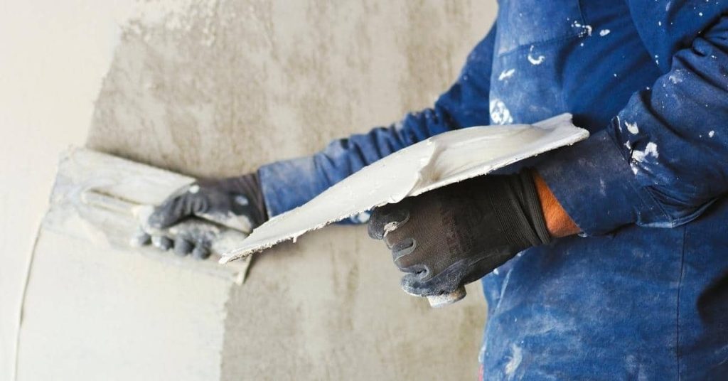 Person applying fresh plaster to wall with trowel and hawk