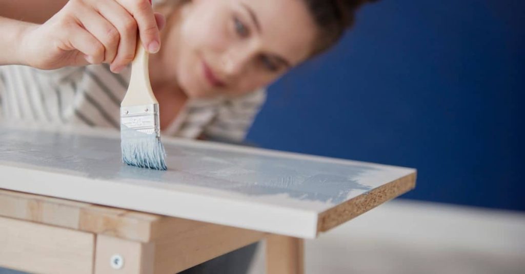 Person applying paint with brush on wood panel