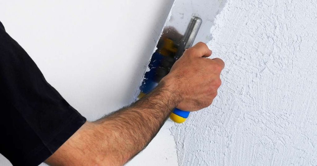 Person applying plaster on wall with trowel
