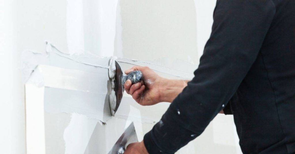 Person applying plaster to drywall seam with putty knife