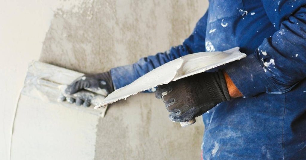 Person applying plaster to wall with trowel and hawk